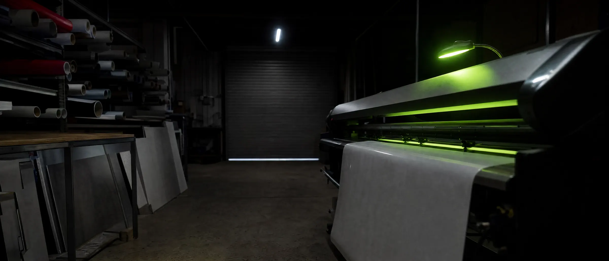 A sign shop workshop at night, large-format printer mid-print.